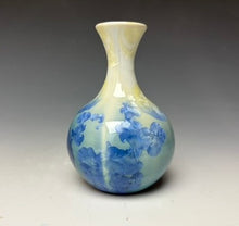 Load image into Gallery viewer, a small porcelain bud vase with a zinc crystalline glaze that has a blue, ivory and cream colored crystals on a grey gradient background