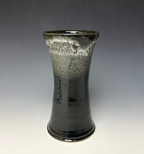 Load image into Gallery viewer, a black vase with light white, foamy looking, area along the top 1/3 of the vase. The vase is pictured on a grey gradient background.