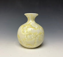 Load image into Gallery viewer, a small porcelain bud vase with a zinc crystalline glaze that has a ivory and cream colored crystals on a grey gradient background