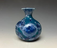 Load image into Gallery viewer, a small porcelain bud vase with a zinc crystalline glaze that has a deep teal blue base with silver/blue colored crystals on a grey gradient background
