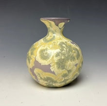 Load image into Gallery viewer, a small porcelain bud vase with a zinc crystalline glaze that has a purple base and cream and grey colored crystals on a grey gradient background
