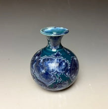 Load image into Gallery viewer, a small porcelain bud vase with a zinc crystalline glaze that has a deep teal blue base with silver/blue colored crystals on a grey gradient background
