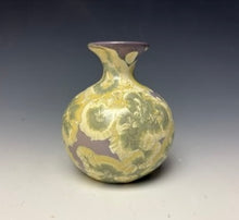 Load image into Gallery viewer, a small porcelain bud vase with a zinc crystalline glaze that has a purple base and cream and grey colored crystals on a grey gradient background