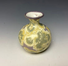 Load image into Gallery viewer, a small porcelain bud vase with a zinc crystalline glaze that has a purple base and cream and grey colored crystals on a grey gradient background