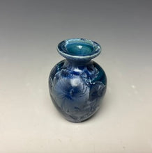 Load image into Gallery viewer, a small porcelain bud vase with a zinc crystalline glaze that has a deep teal blue base with silver/blue colored crystals on a grey gradient background