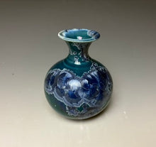 Load image into Gallery viewer, a small porcelain bud vase with a zinc crystalline glaze that has a deep teal blue base with silver/blue colored crystals on a grey gradient background