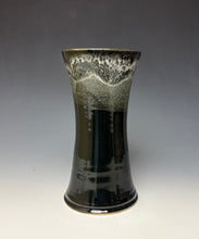 Load image into Gallery viewer, a black vase with light white, foamy looking, area along the top 1/3 of the vase. The vase is pictured on a grey gradient background.