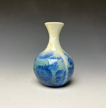 Load image into Gallery viewer, a small porcelain bud vase with a zinc crystalline glaze that has a blue, ivory and cream colored crystals on a grey gradient background