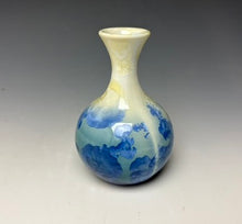 Load image into Gallery viewer, a small porcelain bud vase with a zinc crystalline glaze that has a blue, ivory and cream colored crystals on a grey gradient background