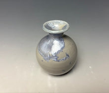 Load image into Gallery viewer, a small porcelain bud vase with a zinc crystalline glaze that has a light lavender colored crystals on a grey gradient background