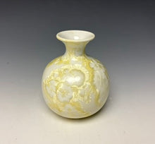 Load image into Gallery viewer, a small porcelain bud vase with a zinc crystalline glaze that has a ivory and cream colored crystals on a grey gradient background