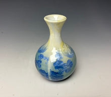 Load image into Gallery viewer, a small porcelain bud vase with a zinc crystalline glaze that has a blue, ivory and cream colored crystals on a grey gradient background
