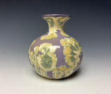 Load image into Gallery viewer, a small porcelain bud vase with a zinc crystalline glaze that has a a purple base with cream/grey colored crystals on a grey gradient background
