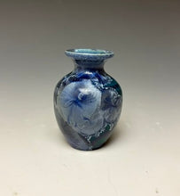 Load image into Gallery viewer, a small porcelain bud vase with a zinc crystalline glaze that has a deep teal blue base with silver/blue colored crystals on a grey gradient background
