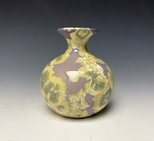 Load image into Gallery viewer, a small porcelain bud vase with a zinc crystalline glaze that has a light lavender base with cream/grey colored crystals on a grey gradient background
