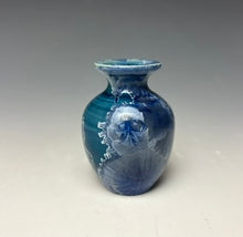 Load image into Gallery viewer, a small porcelain bud vase with a zinc crystalline glaze that has a deep teal blue base with silver/blue colored crystals on a grey gradient background
