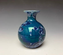 Load image into Gallery viewer, a small porcelain bud vase with a zinc crystalline glaze that has a deep blue colored crystals on a grey gradient background
