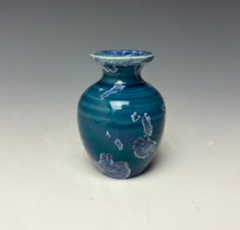 Load image into Gallery viewer, a small porcelain bud vase with a zinc crystalline glaze that has a deep teal blue base with silver/blue colored crystals on a grey gradient background
