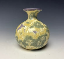 Load image into Gallery viewer, a small porcelain bud vase with a zinc crystalline glaze that has a light lavender base with cream/grey colored crystals on a grey gradient background
