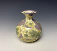 Load image into Gallery viewer, a small porcelain bud vase with a zinc crystalline glaze that has a light lavender base with cream/grey colored crystals on a grey gradient background
