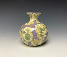 Load image into Gallery viewer, a small porcelain bud vase with a zinc crystalline glaze that has a a purple base with cream/grey colored crystals on a grey gradient background
