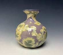 Load image into Gallery viewer, a small porcelain bud vase with a zinc crystalline glaze that has a a purple base with cream/grey colored crystals on a grey gradient background

