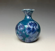 Load image into Gallery viewer, a small porcelain bud vase with a zinc crystalline glaze that has a deep teal blue base with silver/blue colored crystals on a grey gradient background
