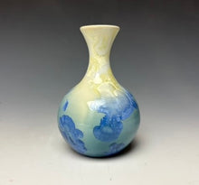 Load image into Gallery viewer, a small porcelain bud vase with a zinc crystalline glaze that has a blue, ivory and cream colored crystals on a grey gradient background

