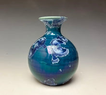 Load image into Gallery viewer, a small porcelain bud vase with a zinc crystalline glaze that has a deep blue colored crystals on a grey gradient background
