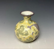 Load image into Gallery viewer, a small porcelain bud vase with a zinc crystalline glaze that has a purple base and cream and grey colored crystals on a grey gradient background

