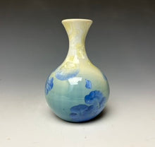 Load image into Gallery viewer, a small porcelain bud vase with a zinc crystalline glaze that has a blue, ivory and cream colored crystals on a grey gradient background
