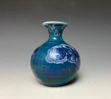 Load image into Gallery viewer, a small porcelain bud vase with a zinc crystalline glaze that has a deep teal blue base with silver/blue colored crystals on a grey gradient background
