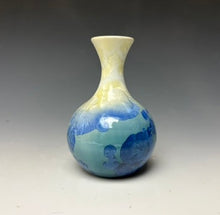Load image into Gallery viewer, a small porcelain bud vase with a zinc crystalline glaze that has a blue, ivory and cream colored crystals on a grey gradient background
