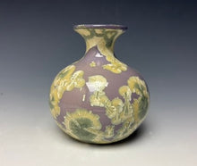 Load image into Gallery viewer, a small porcelain bud vase with a zinc crystalline glaze that has a a purple base with cream/grey colored crystals on a grey gradient background
