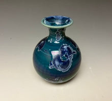 Load image into Gallery viewer, a small porcelain bud vase with a zinc crystalline glaze that has a deep blue colored crystals on a grey gradient background
