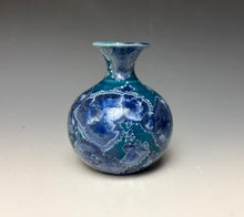 Load image into Gallery viewer, a small porcelain bud vase with a zinc crystalline glaze that has a deep teal blue base with silver/blue colored crystals on a grey gradient background
