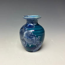 Load image into Gallery viewer, a small porcelain bud vase with a zinc crystalline glaze that has a deep teal blue base with silver/blue colored crystals on a grey gradient background
